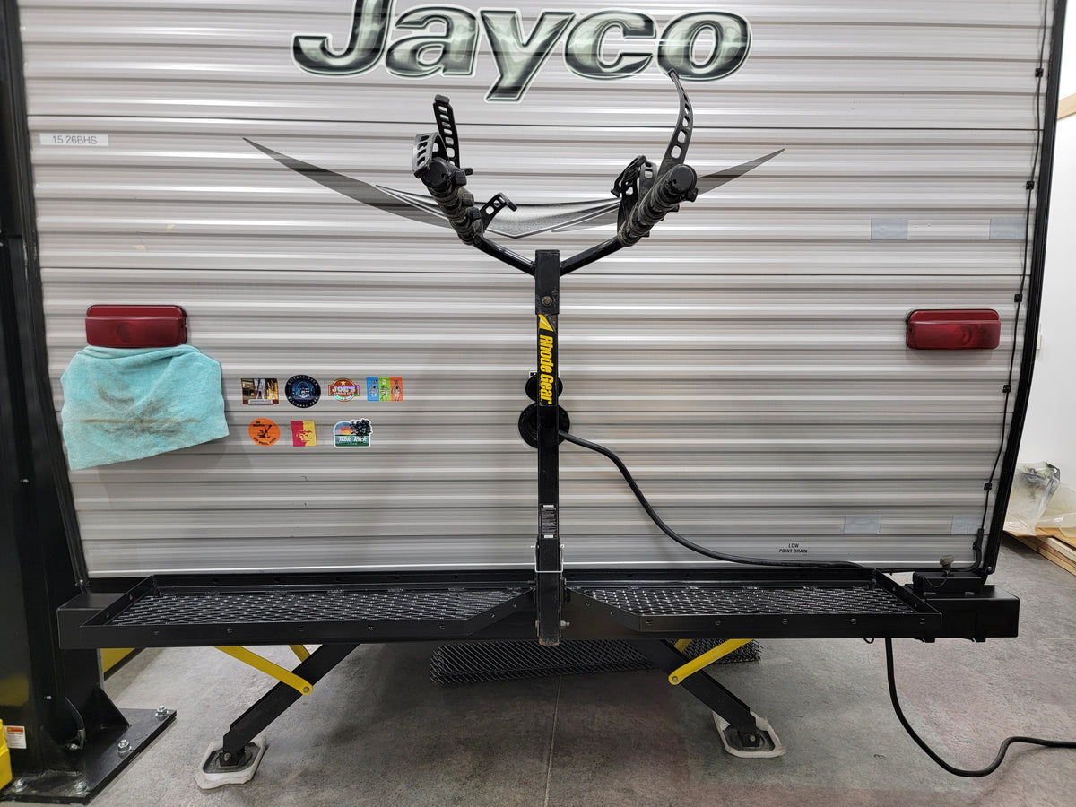 Black bike rack attached to a Jayco RV in a garage setting