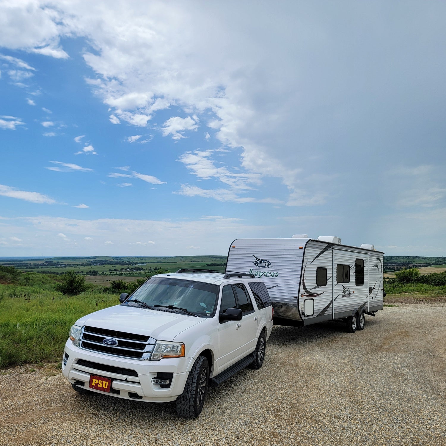 White SUV towing a travel trailer on a dirt road with a scenic background