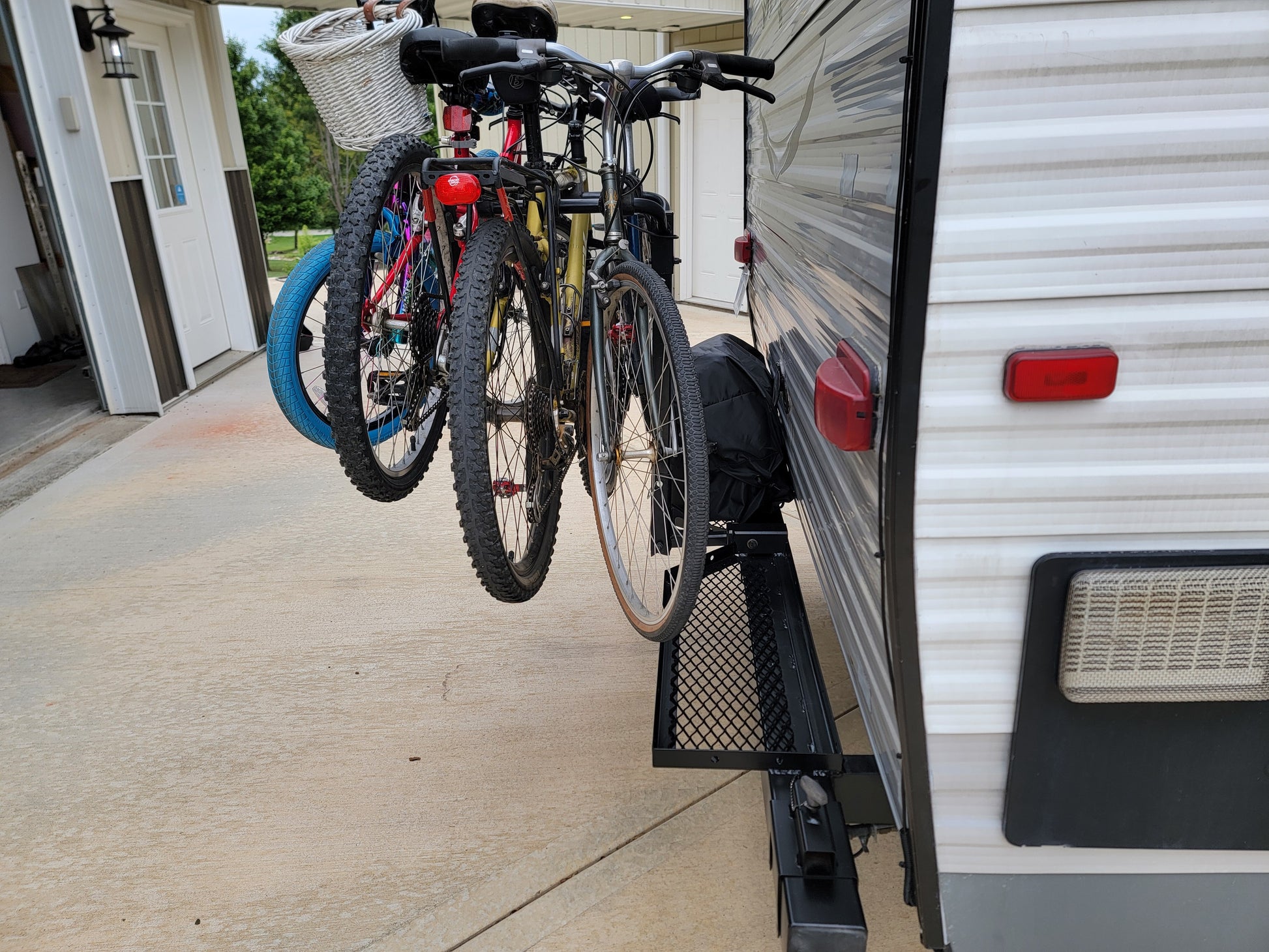 Bicycles attached to a trailer hitch of an RV on a driveway.