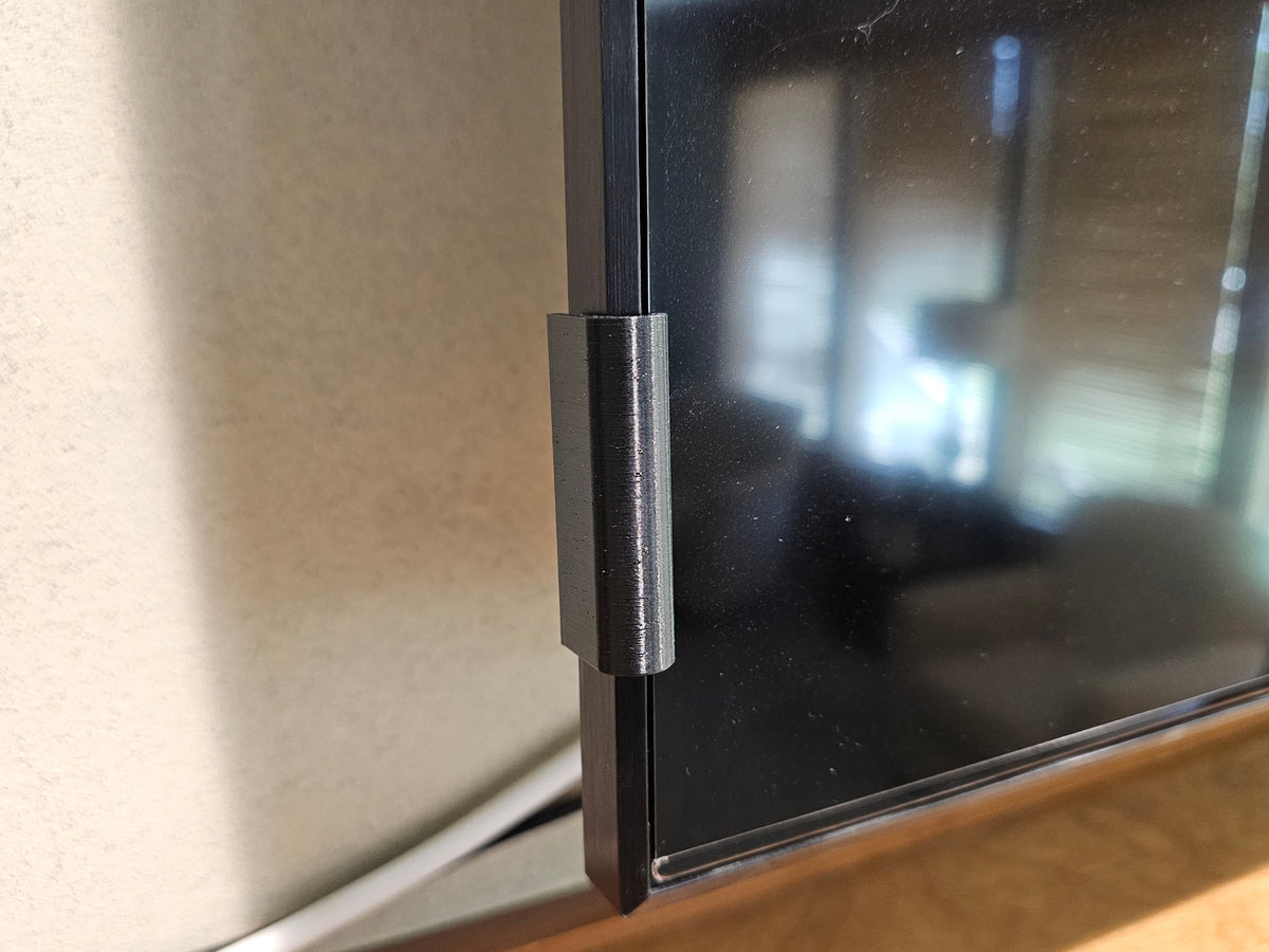 Close-up of a black stick-on TV screen retention clip holding the screen edge