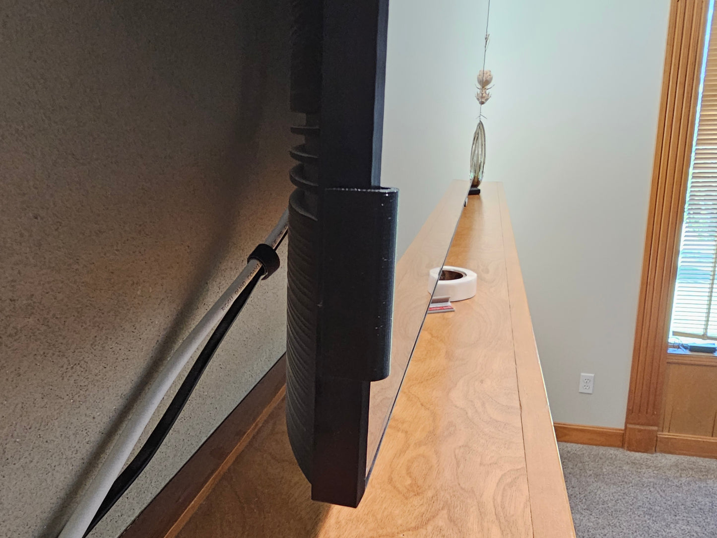 Rear view of a black adhesive TV screen retention clip installed on the television frame